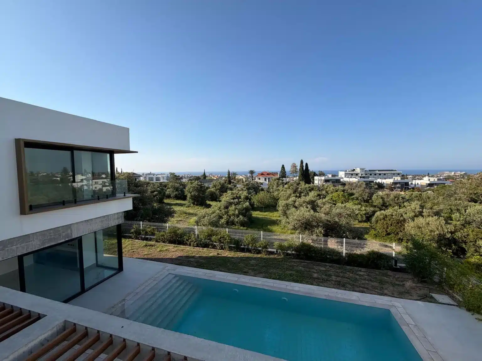 Blick von oben auf den Privatpool einer modernen Villa mit großen Glasfronten und grüner Umgebung