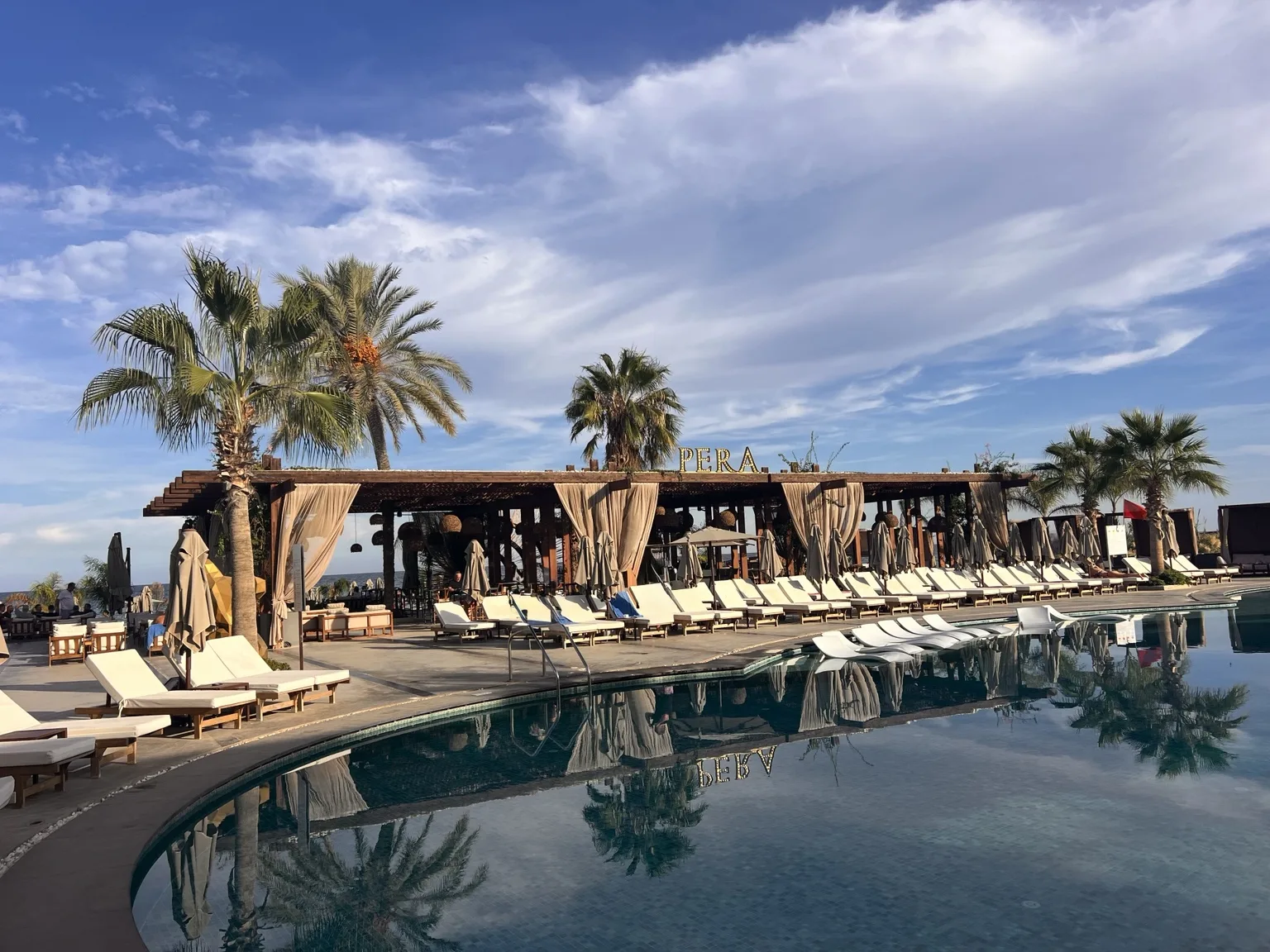 Pool mit Palmen und Liegebereichen im Pera Beach Club am Long Beach